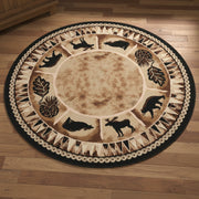 A round area rug with a rustic woodland theme, featuring black silhouettes of various deer, bears, and a moose around a tan center, surrounded by pinecones and leaves, and finished with a black and beige patterned border.