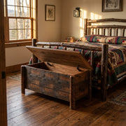 Atlantic Peak Barnwood Blanket Chest with its lid open at the foot of a log bed in a sunlit farmhouse bedroom