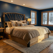Huron Peak Hickory Sunburst Platform Bed with tan bedding against a deep blue wall in a cabin bedroom with snowy forest windows