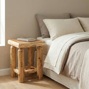Mount Bancroft Cedar Log Open Nightstand in Natural beside a bed with cream bedding and a stack of books