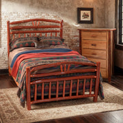 Mount Columbia Hickory Wagon Wheel Bed with a red striped blanket beside a pine dresser in a rustic bedroom with a stone wall