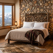 Mount Eolus Hickory Log Twig Headboard against a river rock wall with a snowy mountain window view and a cowhide rug