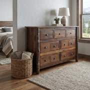 Mount Oklahoma Barnwood and Hickory Dresser beside a bed with a woven basket and table lamp in a bright bedroom