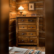 Mount Tweto Reclaimed Barnwood Chest of Drawers with an oil lamp on top against log walls in a rustic cabin bedroom