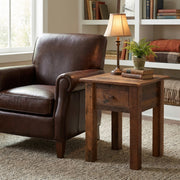 Paiute Peak Reclaimed Barnwood One Drawer End Table beside a leather armchair with a table lamp