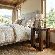 Rosalie Peak Reclaimed Barnwood Open Nightstand with a table lamp beside a bed with white bedding near a mountain-view window
