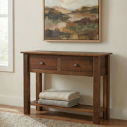 Thatchtop Mountain Reclaimed Barnwood Two Drawer Sofa Table below a landscape painting with folded blankets on the shelf