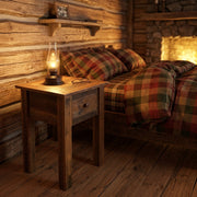Treasure Mountain Reclaimed Barnwood Nightstand with a lantern beside a plaid bed and fireplace in a cabin bedroom