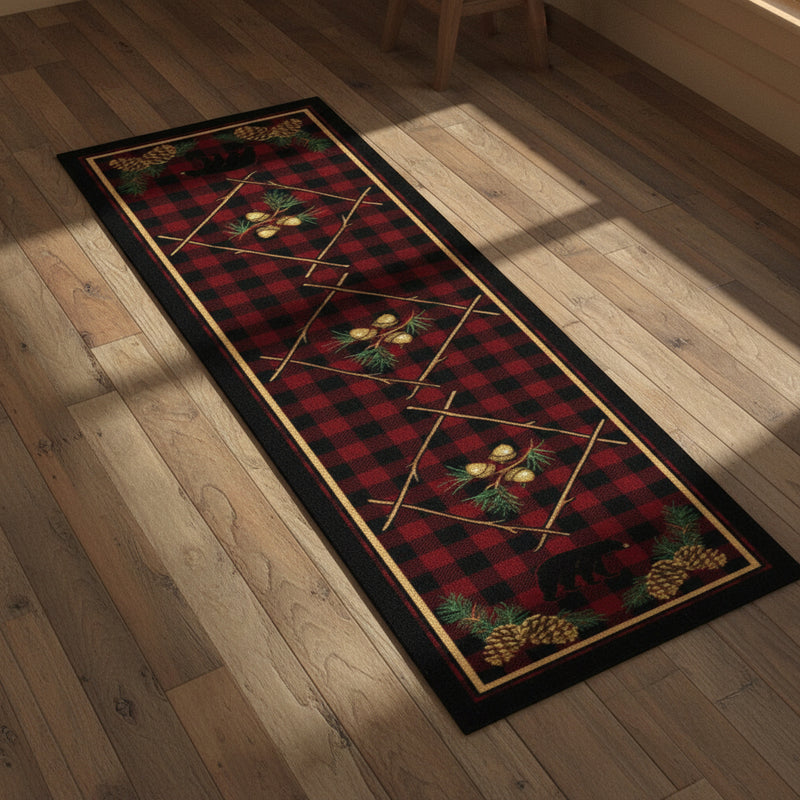 A vertical rectangular runner rug with a red and black buffalo plaid pattern, decorated with pine branches, pinecones, acorns, and black bear silhouettes at the top and bottom.